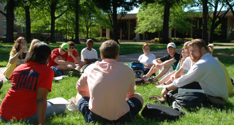 Weber with students seated in grass in a discussion.