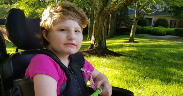 This is a photo of my daughter, Helen, that I took in 2019. She is sitting in her wheelchair on a sunny day, awaiting the schoolbus.